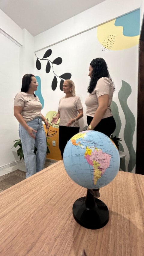 Três profissionais da Conectar conversam no espaço da clínica, ao lado de uma mesa com um globo terrestre.